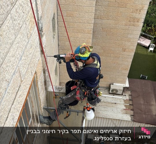 אדם תלוי על חבלים קודח בקיר בניין